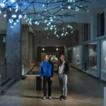 Colour photograph of the artists beneath the Bloom light installation