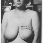 Black and white photograph of a topless Jo Spence with Property of Jo Spence written across her breast