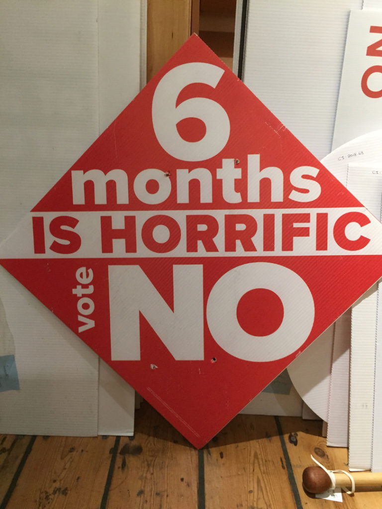A large protest sign reading 6 months is horrific vote no