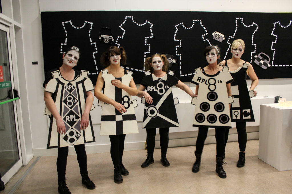 Five women wear black and white cut out doll costumes