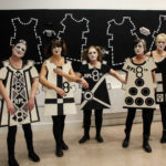 Five women wear black and white cut out doll costumes