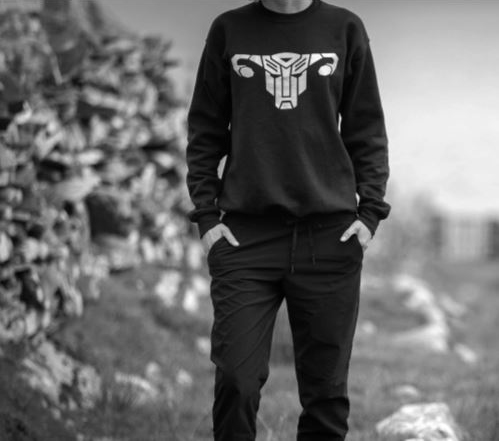 Black and white photograph of someone wearing a sweatshirt with a stylised Transformer logo in the shape of a uterus