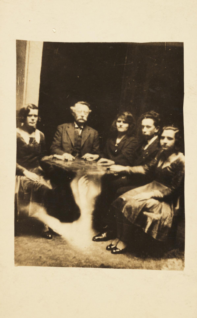 Sepia photograph of a seance showing a spectral hand