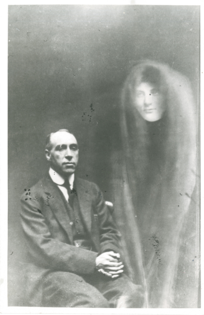 Black and white photograph of a seated man showing a spectral female figure beside him