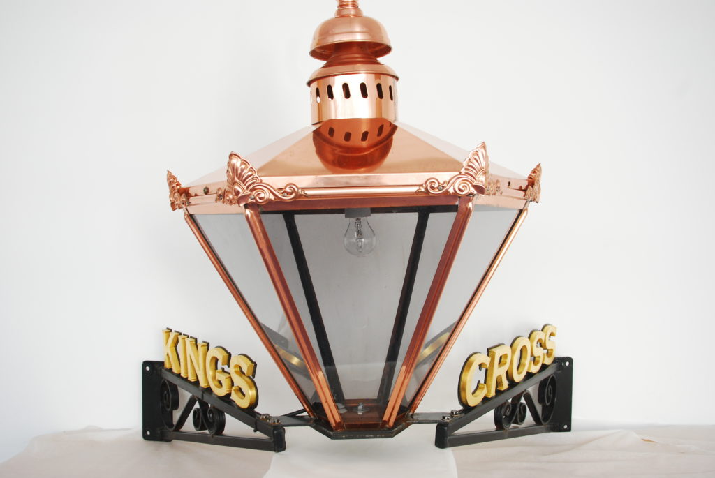 Colour photograph of a copper Victorian style lamp with KINGS CROSS letters in gold