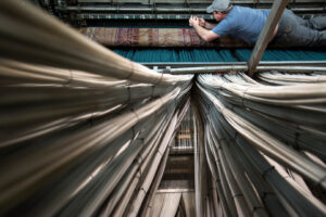 Photograph of a weaver mending a broken thread inside a giant broad loom