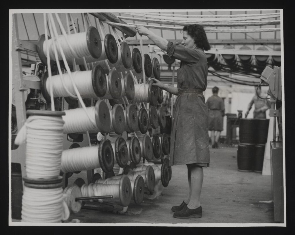 Black and white photograph of a woman working at a weaving machine