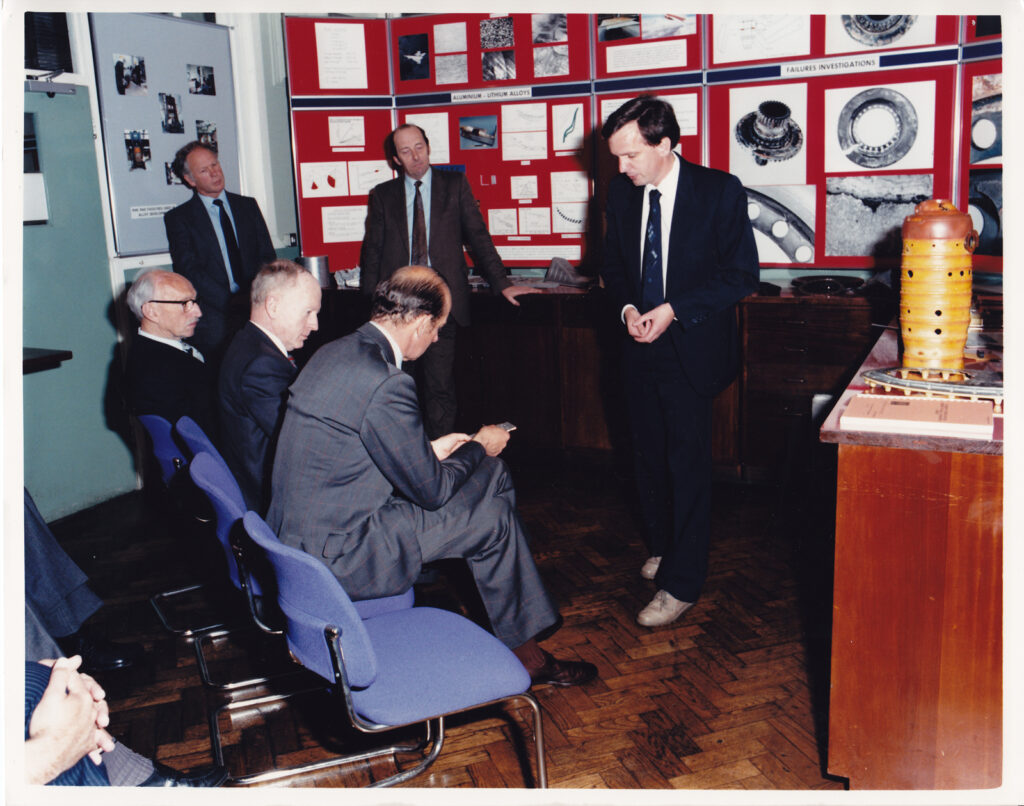 Colour photograph of Chris Peel showing the Duke of Kent components from major aircraft accidents in the Failures Investigations Laboratory at RAE in 1987