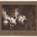 Image of a scanned photograph in sepia tones of a young girl playing with fairies. Caption printed on the brown carboard background says 'A. Alice and the Fairies'