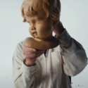 A man holds up a cherubic head sculpted out of wood. Behind, the viewer can see his torso in a white shirt.