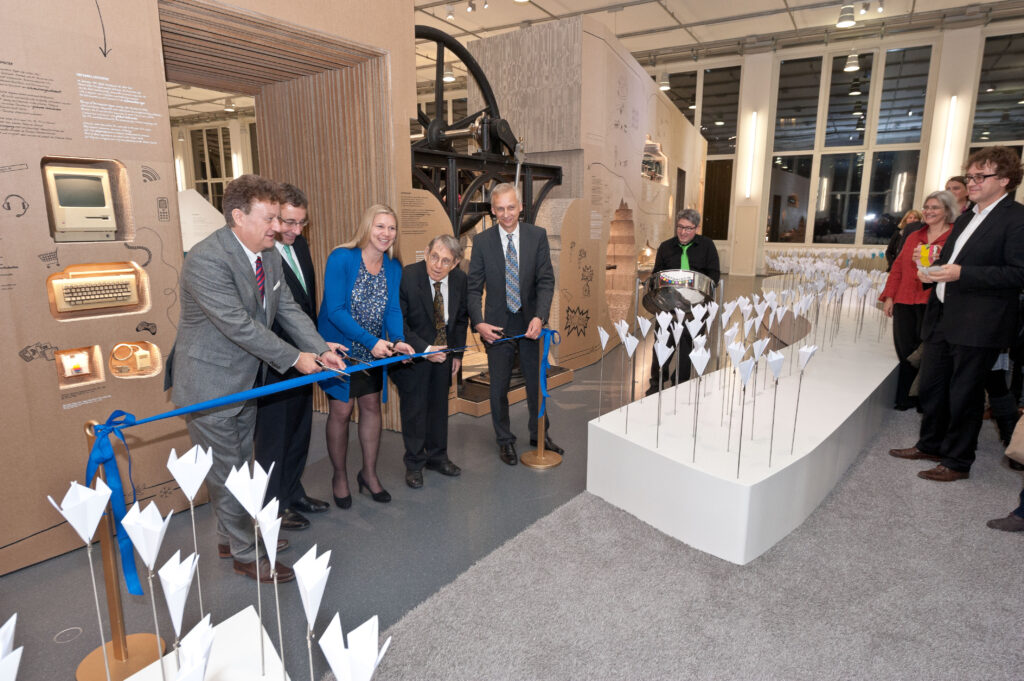 A number of scientists, curators, and public figures cutting a blue ribbon at the opening of a gallery.