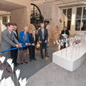 A number of scientists, curators, and public figures cutting a blue ribbon at the opening of a gallery.