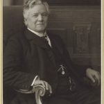 Black and white photograph of a middle aged male doctor sat in an ornate wooden chair
