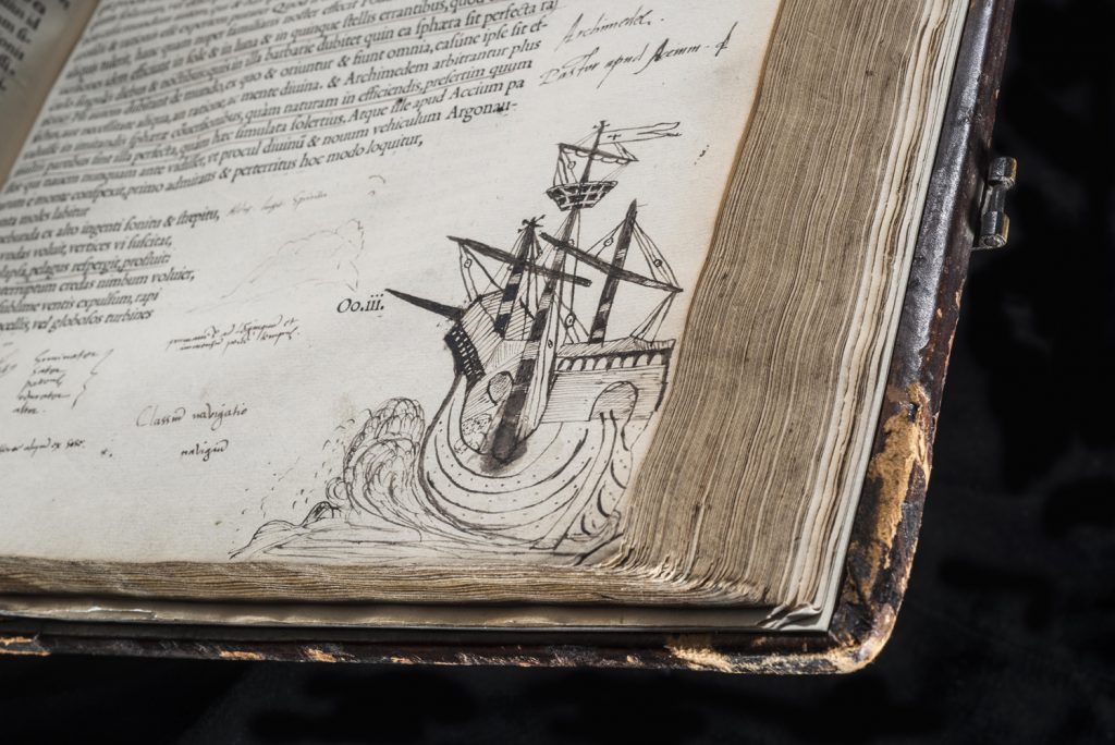 Colour photograph of an ancient book showing a doodle of a ship in ink