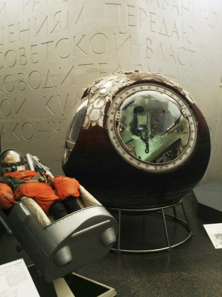 Colour photograph of an early soviet spacesuit next to a spherical descent module