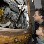 Colour photograph of a man and a boy looking inside the Apollo landing craft on display at the Science Museum London