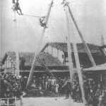Black and white photograph of men erecting electricity pylons watched by a small crowd