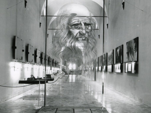 Black and white photograph of a corridor in which are displayed a number of leonardo models paintings and information plaques