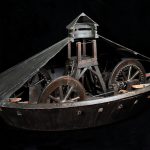 Colour photograph of a wooden model of a covered war chariot with a cut out section showing interior detail