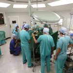 Colour photograph of a simulation based reenactment of a surgical procedure carried out by numerous medical staff