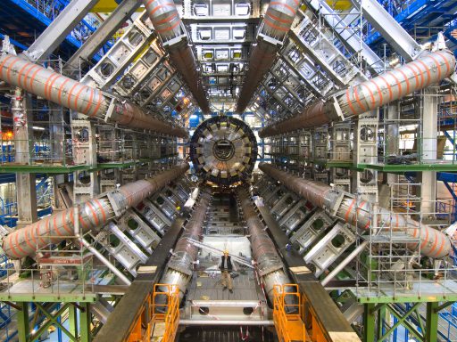 Photograph of the atlas detector during its construction with an engineer standing within its ring structure looking very small in comparison