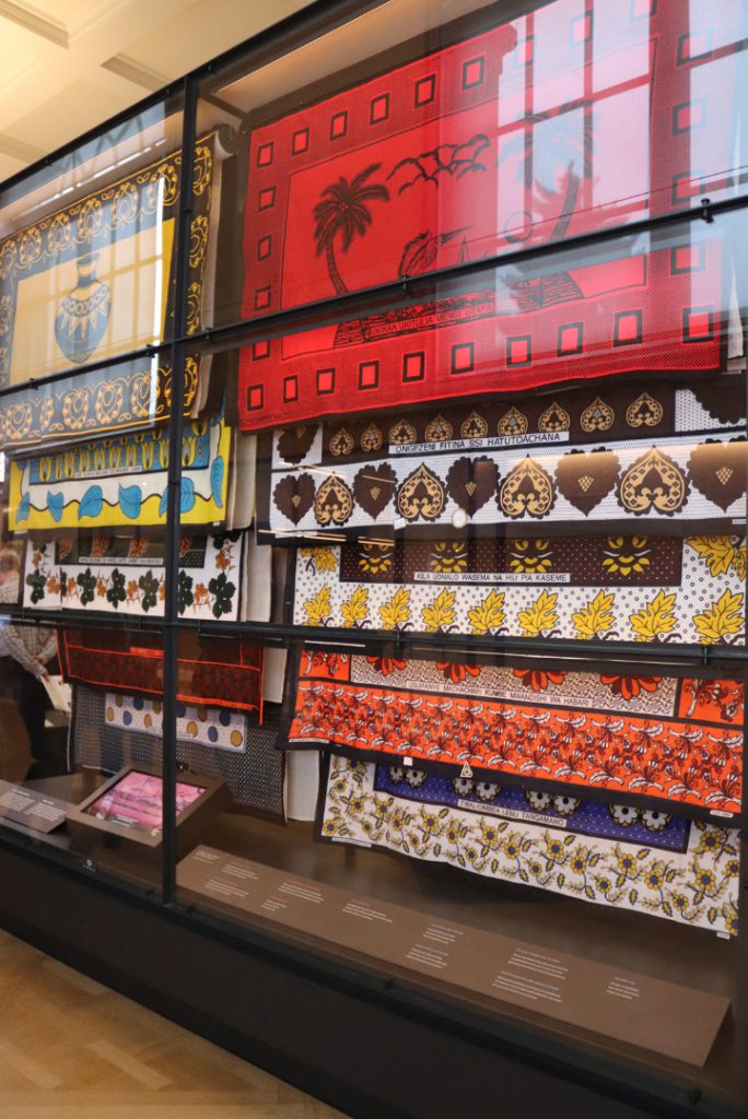 Colour photograph of a museum display case showing different examples of Kanga fabric wraps