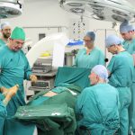 Colour photograph of a simulation based reenactment of a surgical procedure carried out by numerous medical staff