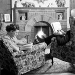 Black and white photograph of a husband and wife sat in front of their living room fire