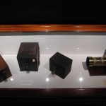 Colour photograph of four early wooden box cameras on display in a glass case