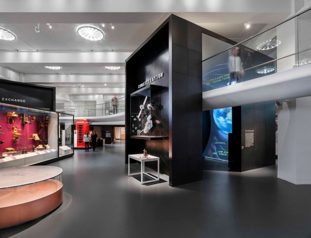Colour photograph of a section of the Information Age gallery showing a constellation display a public telephone box and an aerial walkway which runs around the perimeter of the exhibition