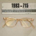 Colour photograph of a pair flesh coloured NHS spectacles