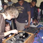 Several members of the National Youth Theatre watch Aleks Kolkowski use an old analogue piece of audio recording kit