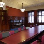 Colour photograph of a long leather topped meeting table with a glass case contained ship model behind