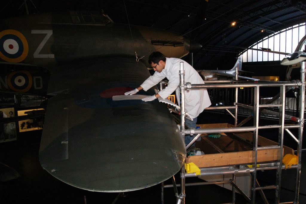 Colour photograph of a conservator repairing a tear on the wing of a Hawker Hurricane aircraft