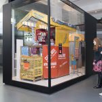 Colour photograph of the connecting Africa display in Information Age showing visitors viewing a mobile phone repair hut from Cameroon