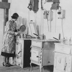 early twentieth century black and white photograph of a woman cooking at a kitchen oven