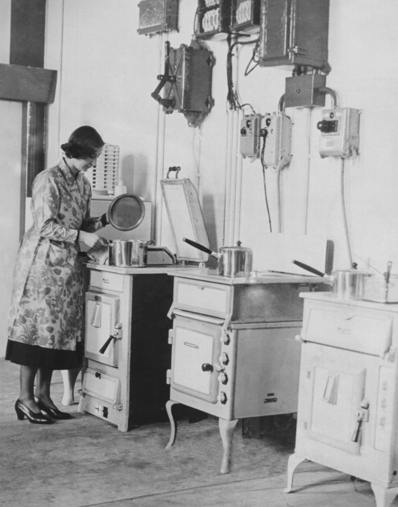 early twentieth century black and white photograph of a woman cooking at a kitchen oven