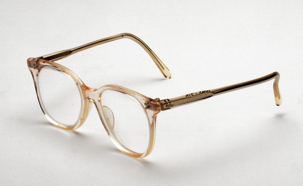 Colour photograph of a pair flesh coloured NHS spectacles