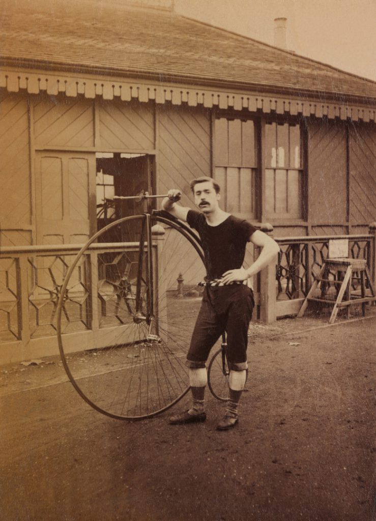 Sepia photograph of a cyclist with his high wheeler bicycle from the late nineteenth century