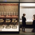 Colour photograph from a high elevation of an old genuine manual telephone exchange desk and two visitors using the adjacent switchboard demonstration console