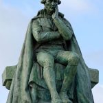 Metallic statue of Jean-Baptiste Lamarck in a sitting pose atop a stone pedestal