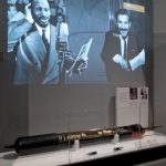 Colour photograph of a transatlantic telephone cable submarine repeater and a large screen above showing an early transatlantic communication