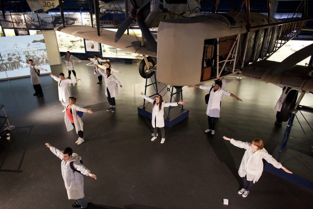 Several members of the National Youth Theatre stand with arms outstretched in the Flight Gallery at the Science Museum