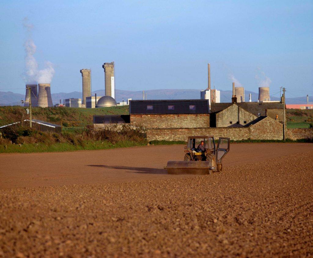 Colour photograph of a field being ploughed with a nuclear power station in the background