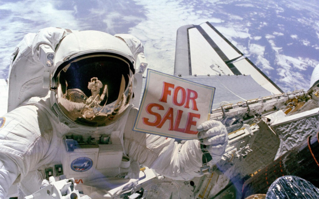 Colour photograph of an astronaut in space floating above a spacecraft and holding up a sign which reads for sale