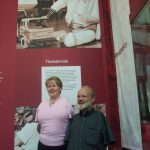 Colour photograph of a male and a female thalidomide patient standing in front of an exhibition display wall