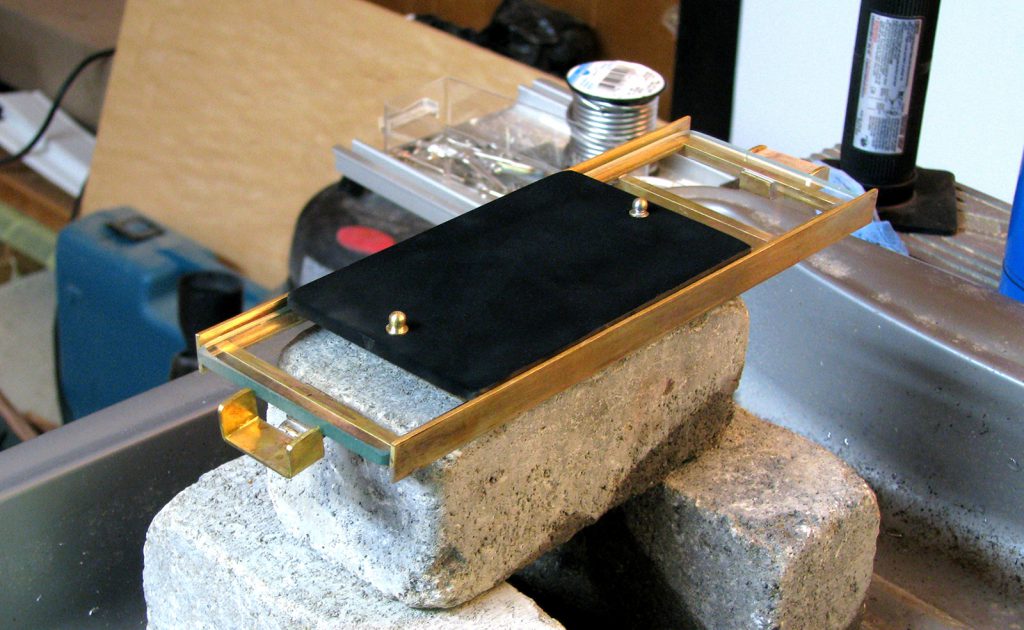 Colour photograph of a glass plate smoked with soot from a candle flame installed on top of the glass bed of the brass stage