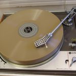 Colour photograph of a freshly recorded wax disc playing on a transcription turntable