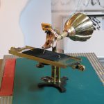 Colour photograph of a 3d printed inner ear attached to a brass mouthpiece and a glass etching plate