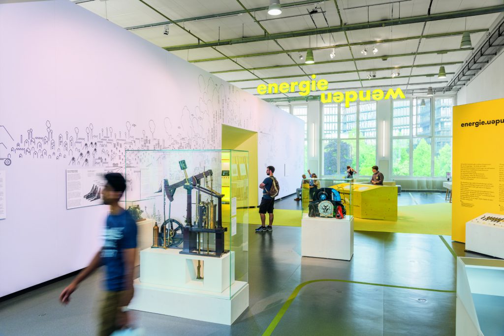 Colour photograph of a bright exhibition space with display objects and visitors